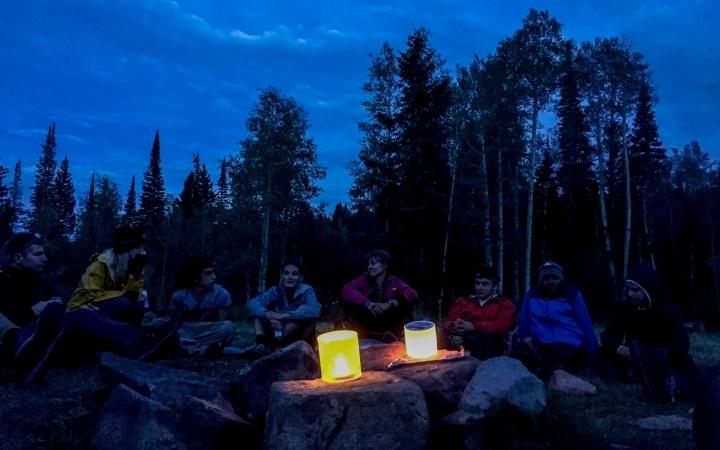 Two lanterns illuminate a group of outward bound students resting at dusk